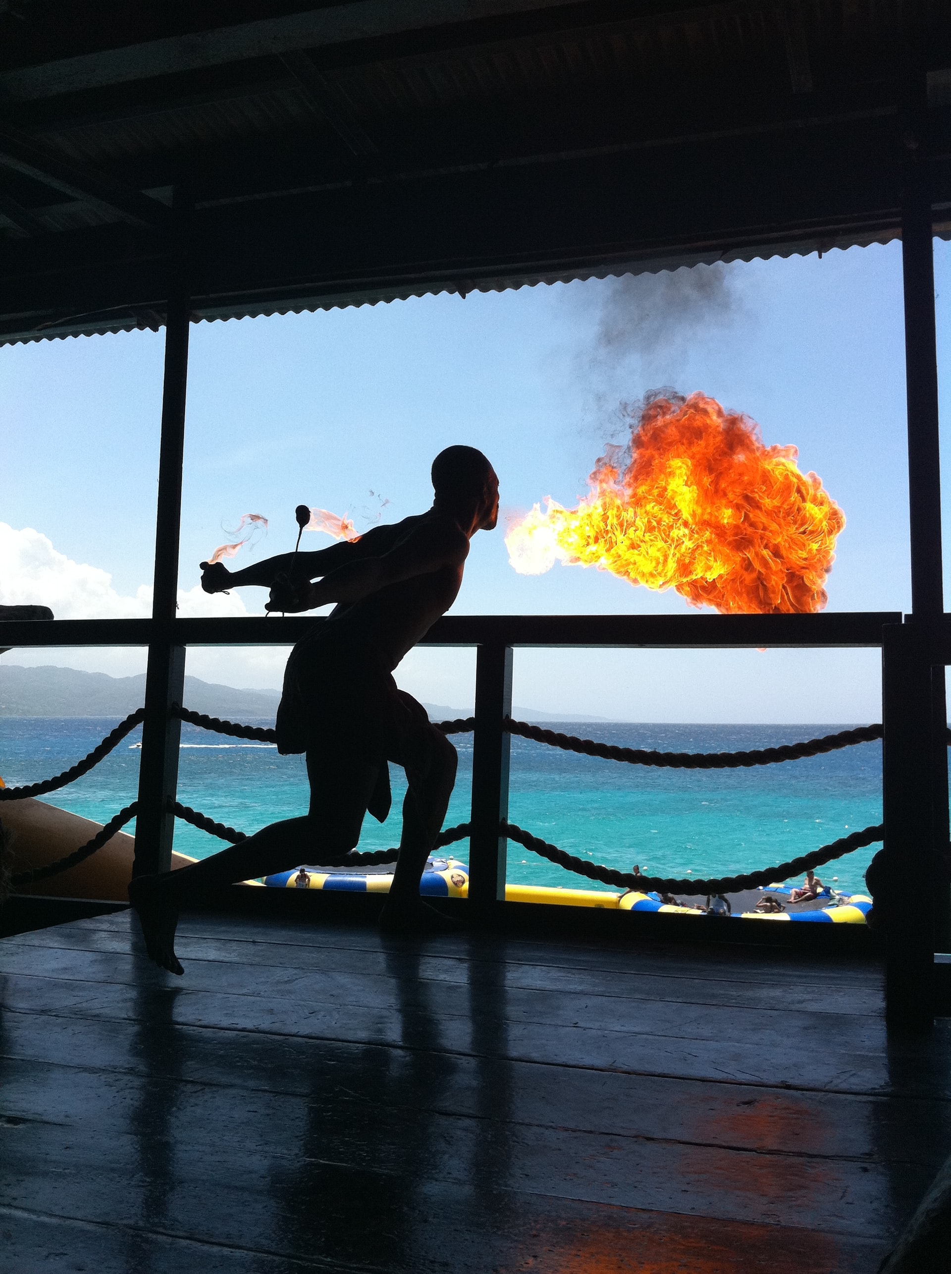 Man breathing fire on wooden stage next to a beach