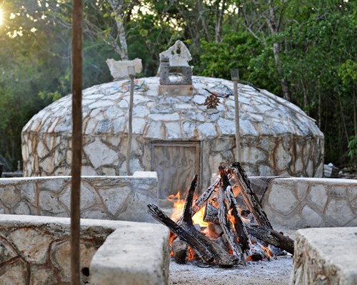 Round stone hut behind an outdoor fire ready for a Temazcal Ceremony