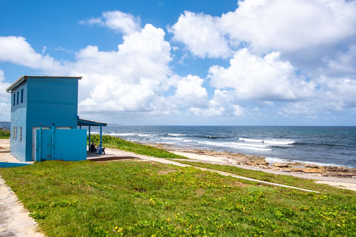 Blue hut on a grassy and rocky beach with wavy sea