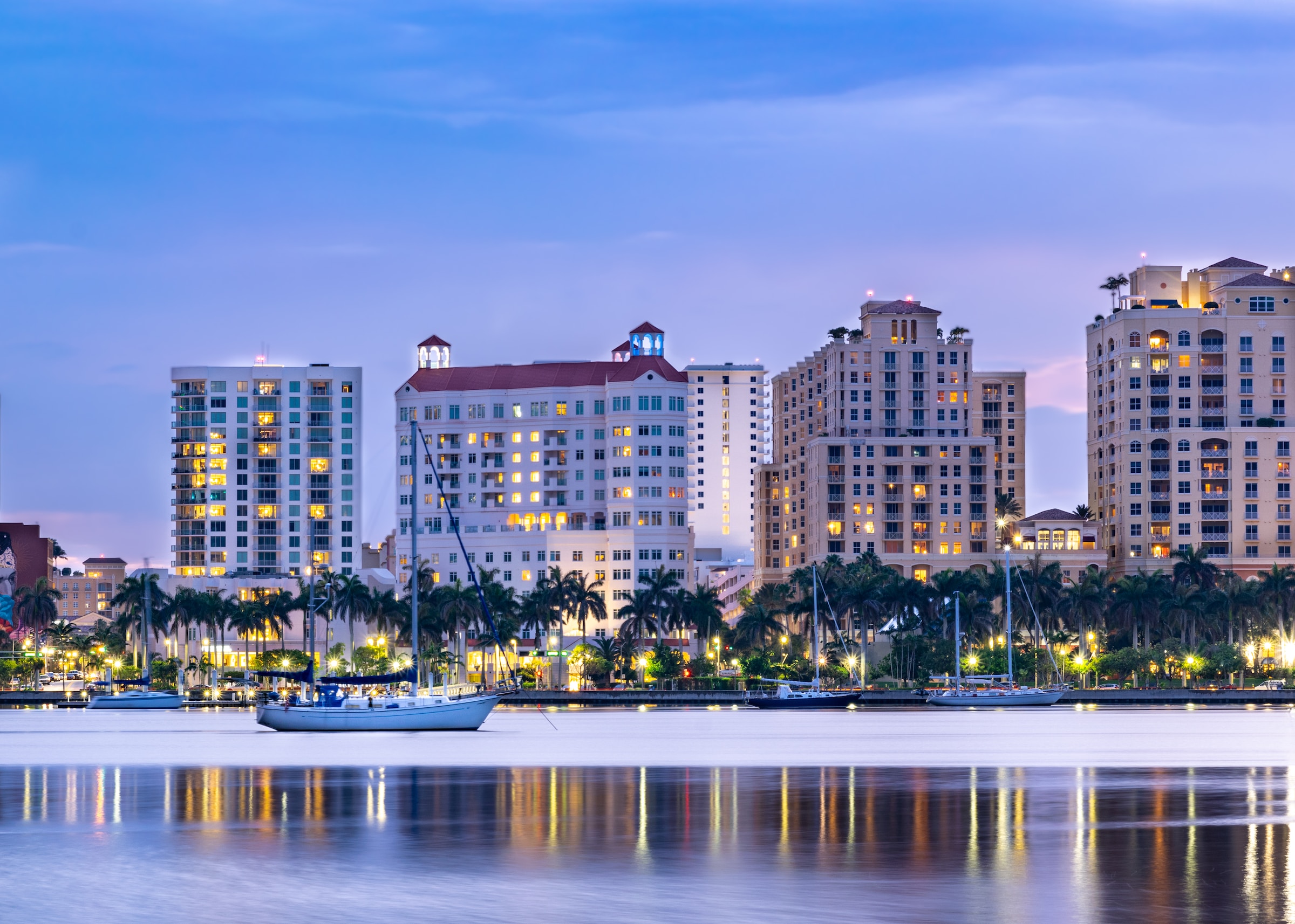 A white boat cruising on water backed by tall buildings