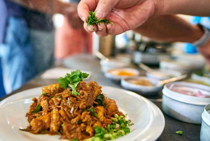 Hand sprinkling green herbs on a curry dish