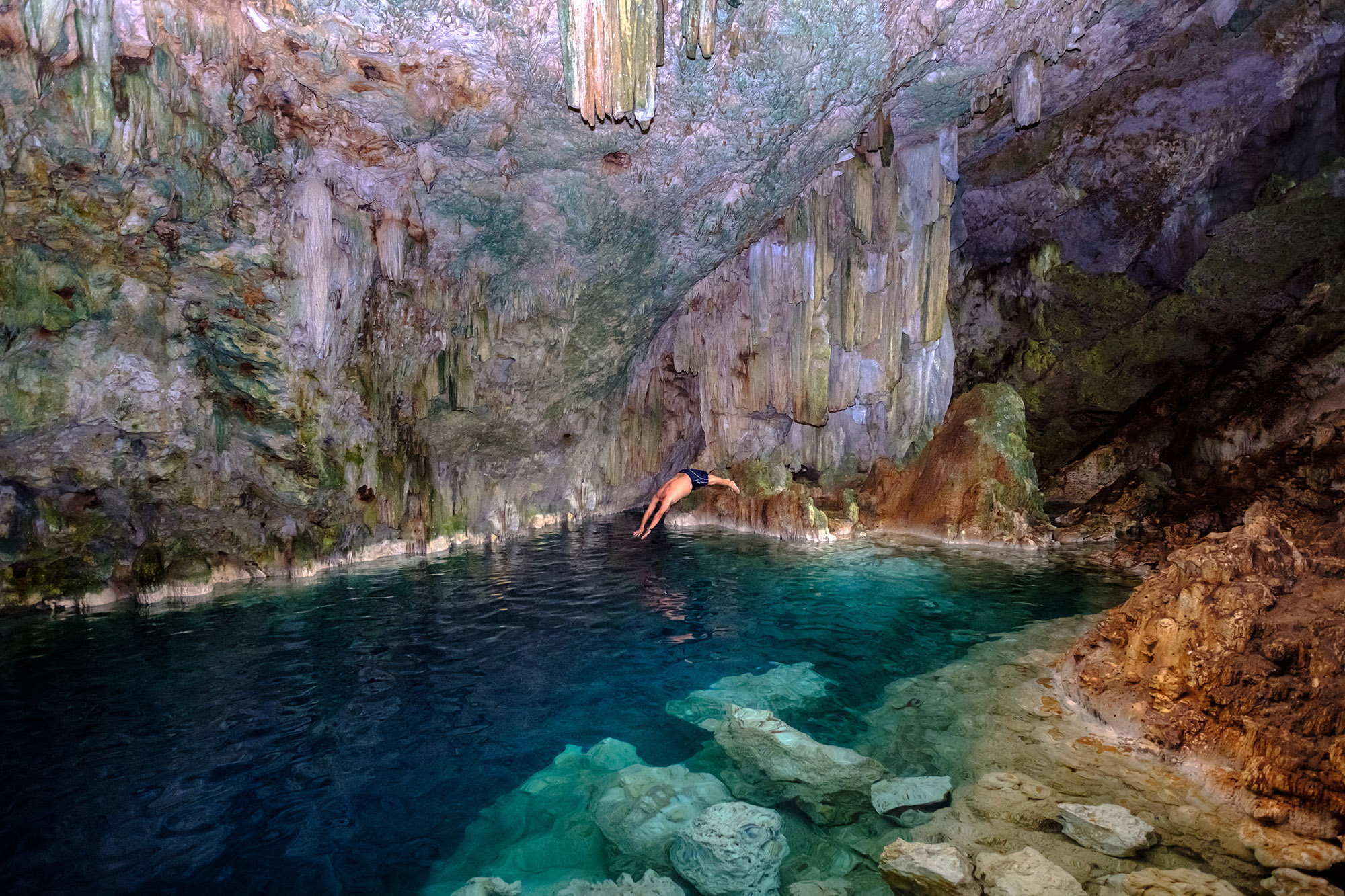 Man diving into a crystal clear freshwater pool in an underground cave
