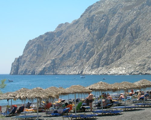 Umbrellas and sun loungers lined up on a beach, backed by tall mountains