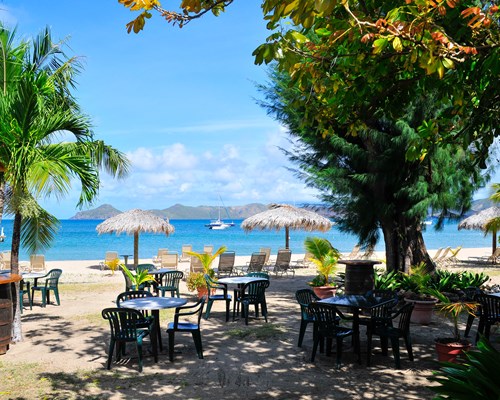 Tables and chair laid out at on a tropical beach with golden sand and several palm trees