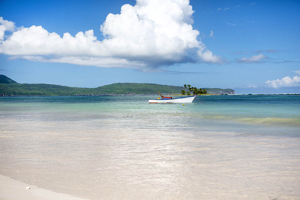 Small, white boat docked up in the bay of a tropical beach