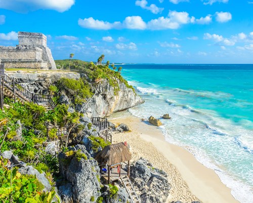 Ruins of a Mayan temple on a cliff next to a beautiful tropical beach with white sand