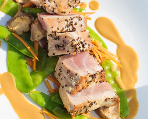 Seasoned, sliced meat on a plate with green beans and sauce