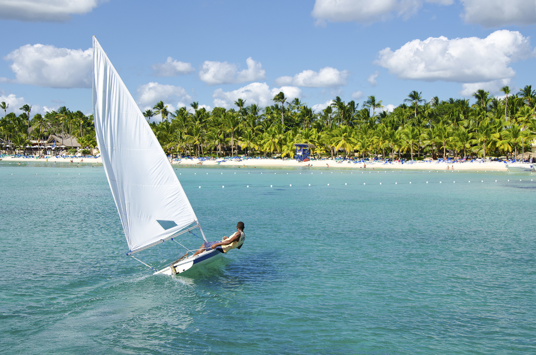 Solo sailing boat near the coast of a white sand tropical beach