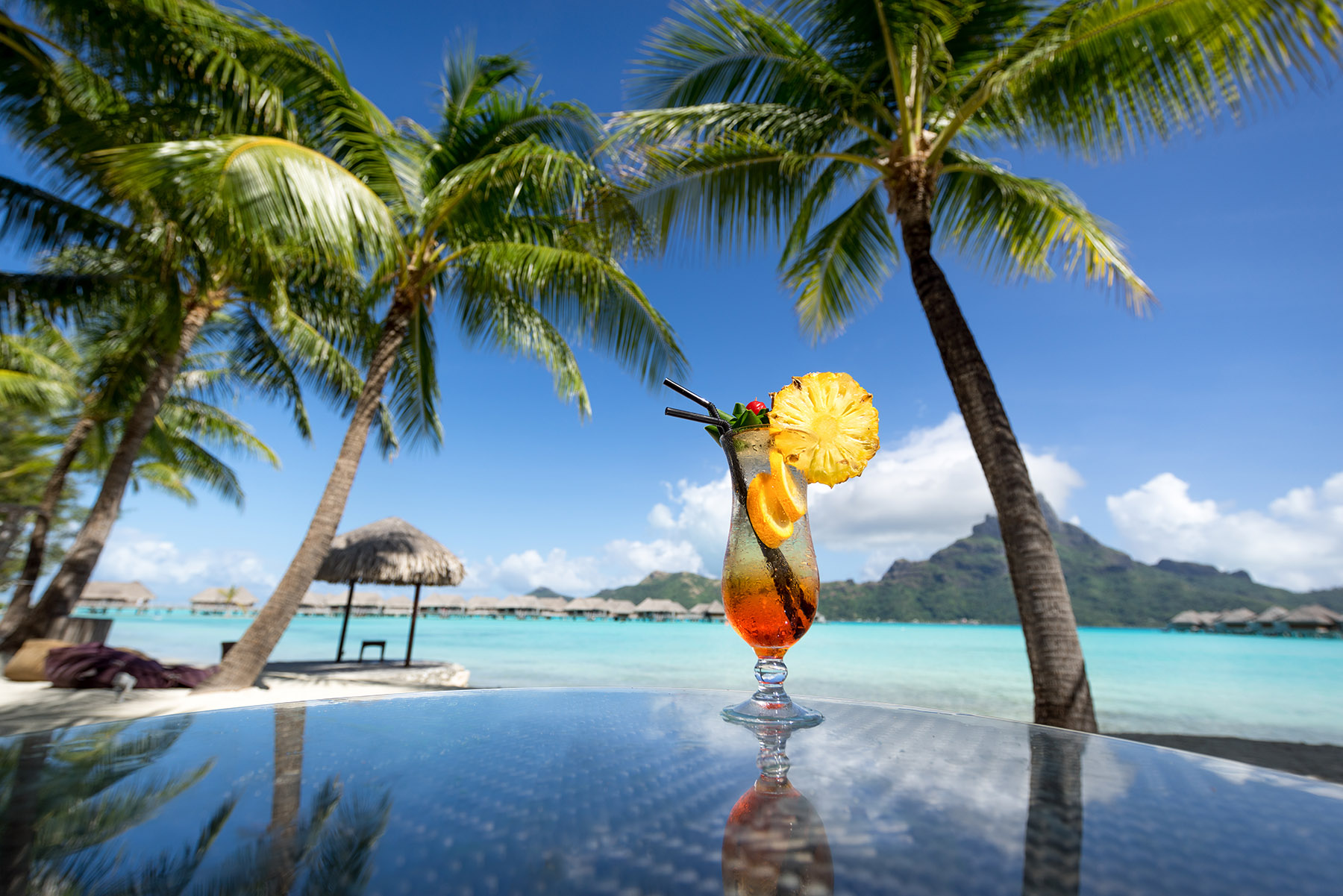 orange cocktail on edge of pool next to beach with palm trees