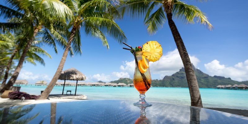 Orange Cocktail Placed On The Ledge Of A Pool Next To Beach