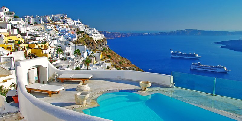 Small white buildings covering a hill overlooking bright blue sea