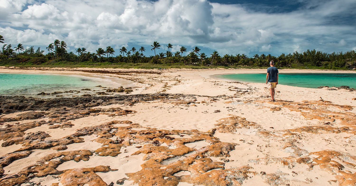 Man walking on a beach between two tropical coves 